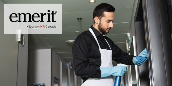 The image shows a worker wearing a black shirt, white apron, and blue gloves, cleaning a surface with a spray bottle in a professional environment. The person appears focused on their task. In the upper left corner, the logo for "emerit" by Tourism HR Canada is displayed, suggesting a connection to training or certification in the tourism or hospitality sector.