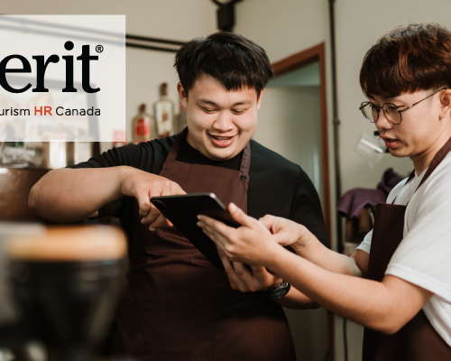 Two café employees wearing brown aprons are smiling and discussing an order while using a tablet. One employee is pointing at the screen while the other listens attentively. The 'emerit by Tourism HR Canada' logo is displayed in the top left corner.
